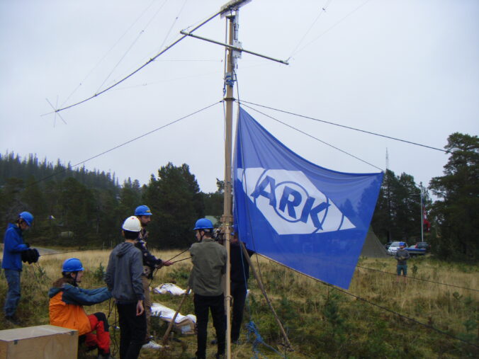 People putting up an antenna with a big ARK flag on it.